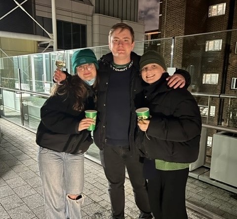 three young adults wearing dark winter clothing standing outdoors