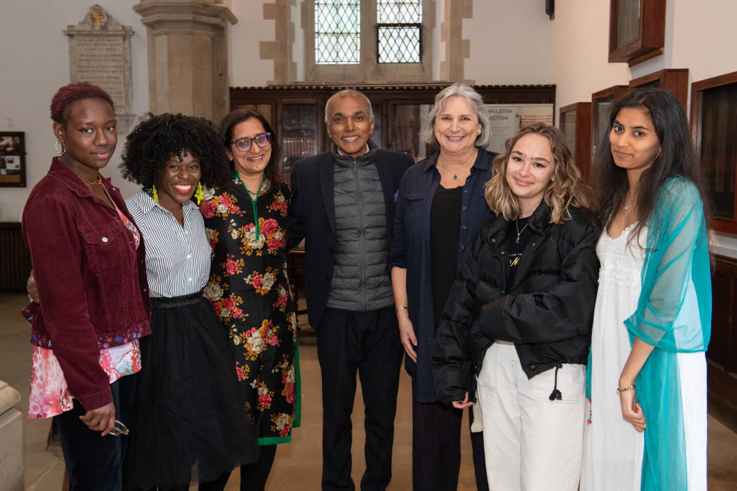 Seven people standing together indoors and smiling