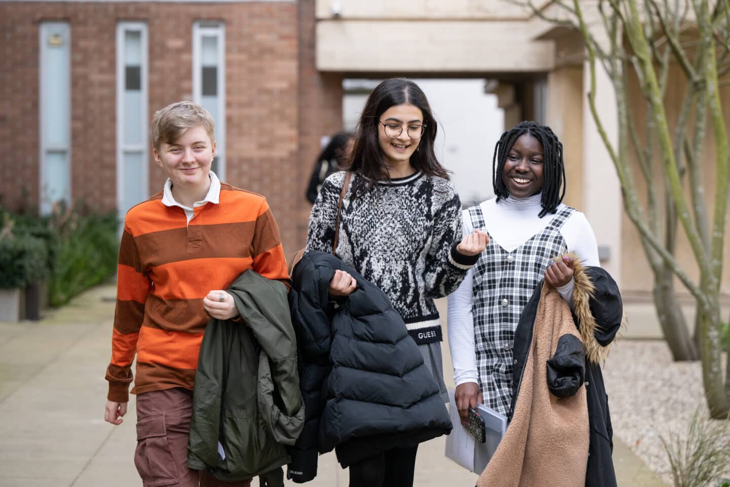 Three young people carrying coats and walking whilst speaking outdoors