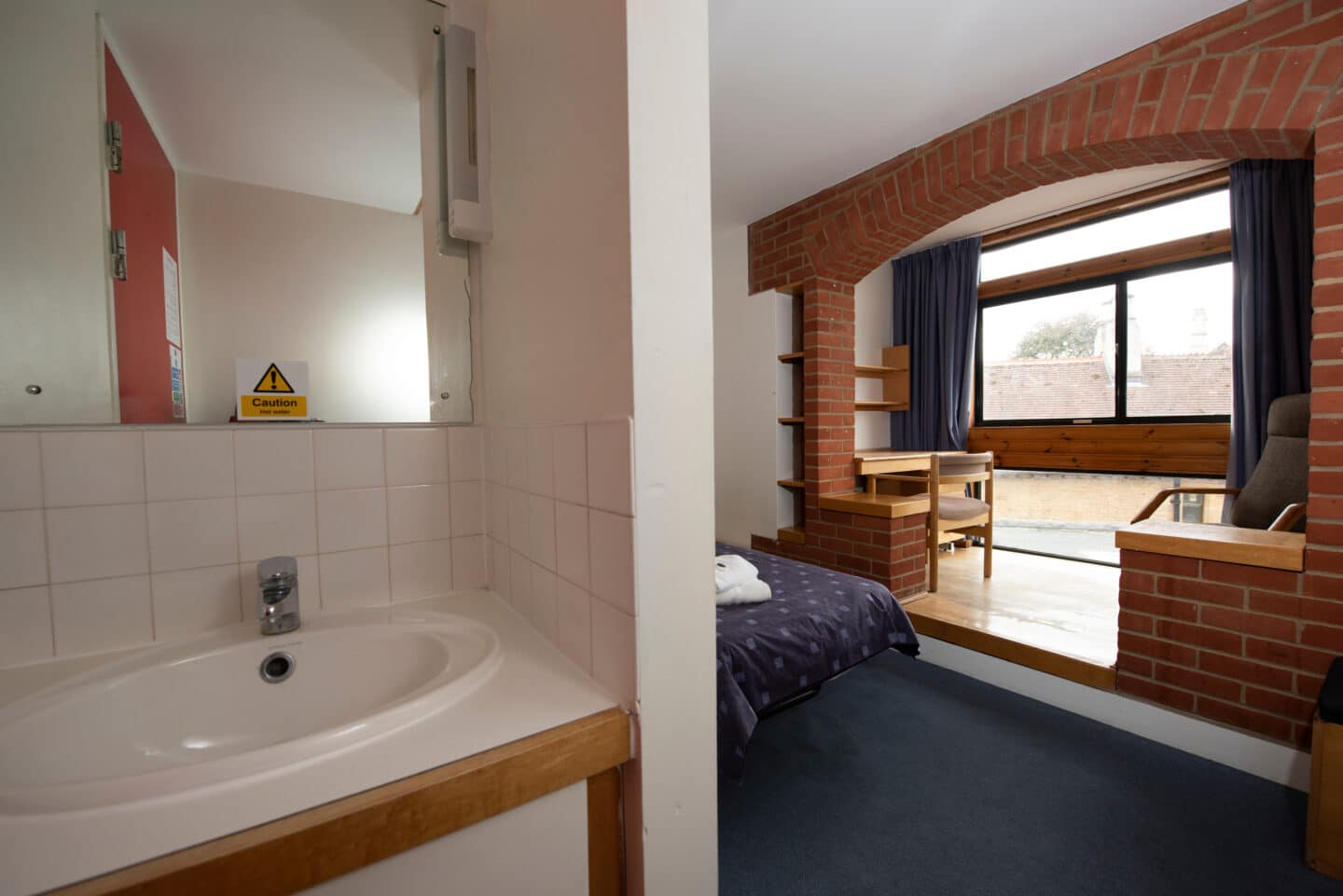 Study bedroom with sink and mirror, bed and desk in front of the window