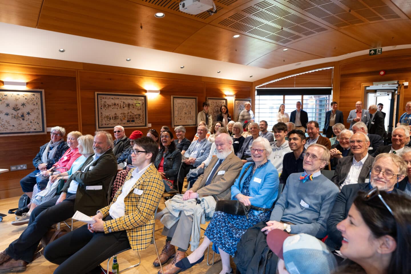 a packed-out lecture room filled with smiling seated guests