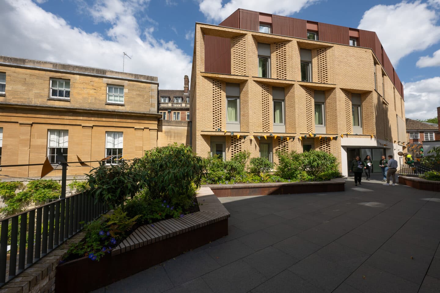 A light brick building surrounded by a garden and patio