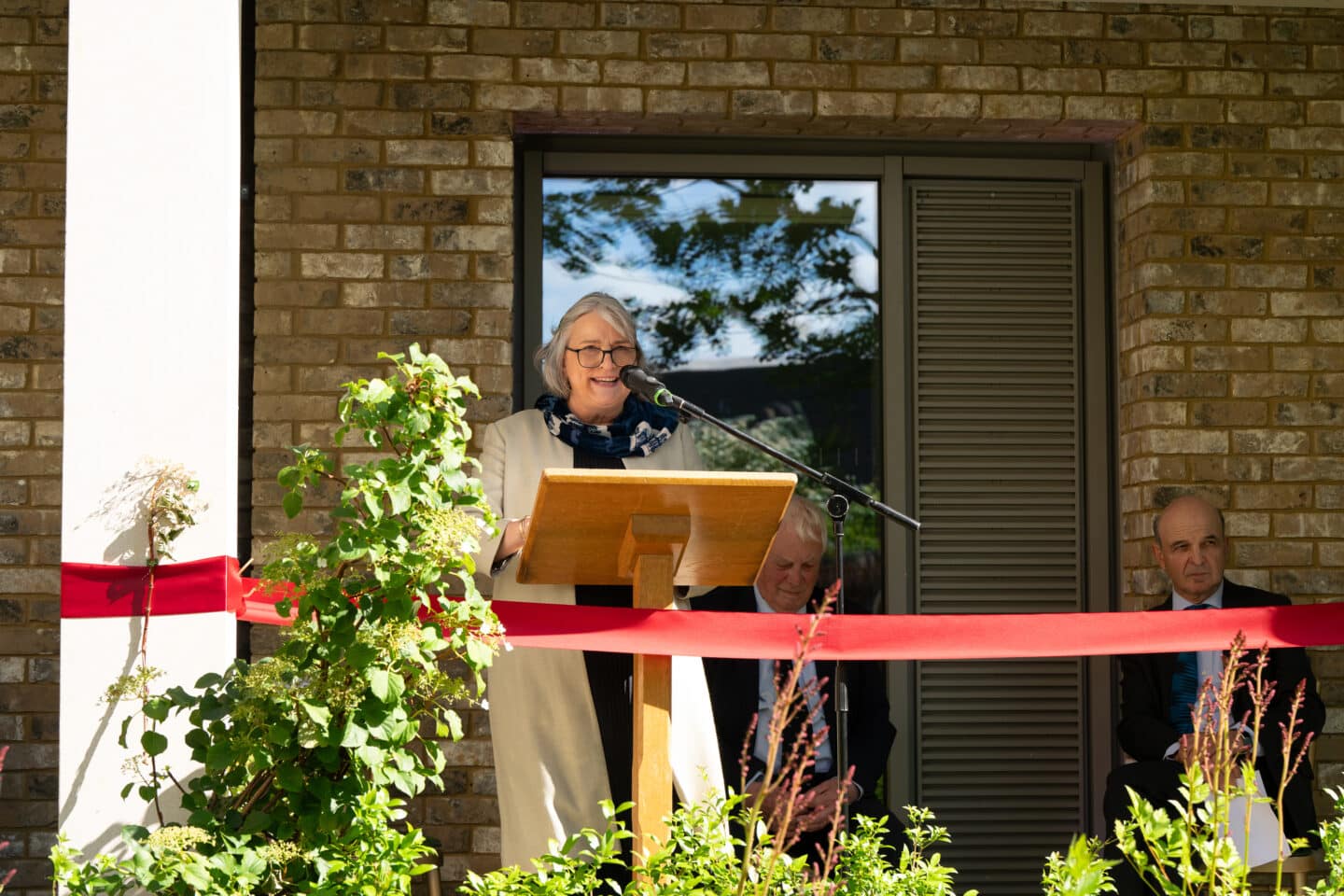 A woman standing on an outdoor stage speaking into a microphone