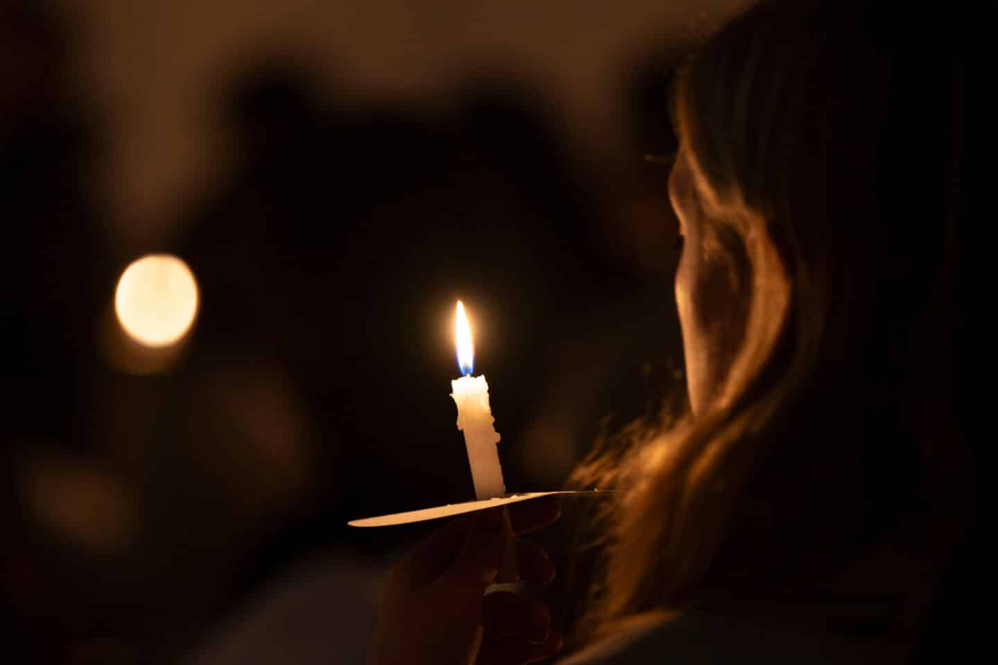 A person with long hair holding a candle in a dark space