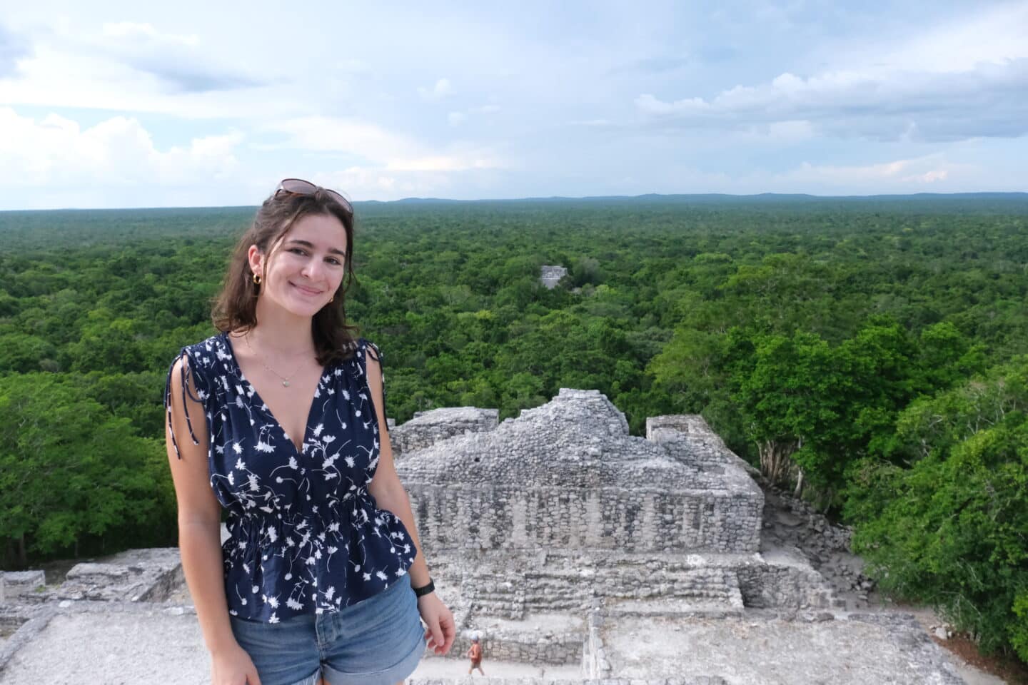 A young person standing on a stone monument above a forest