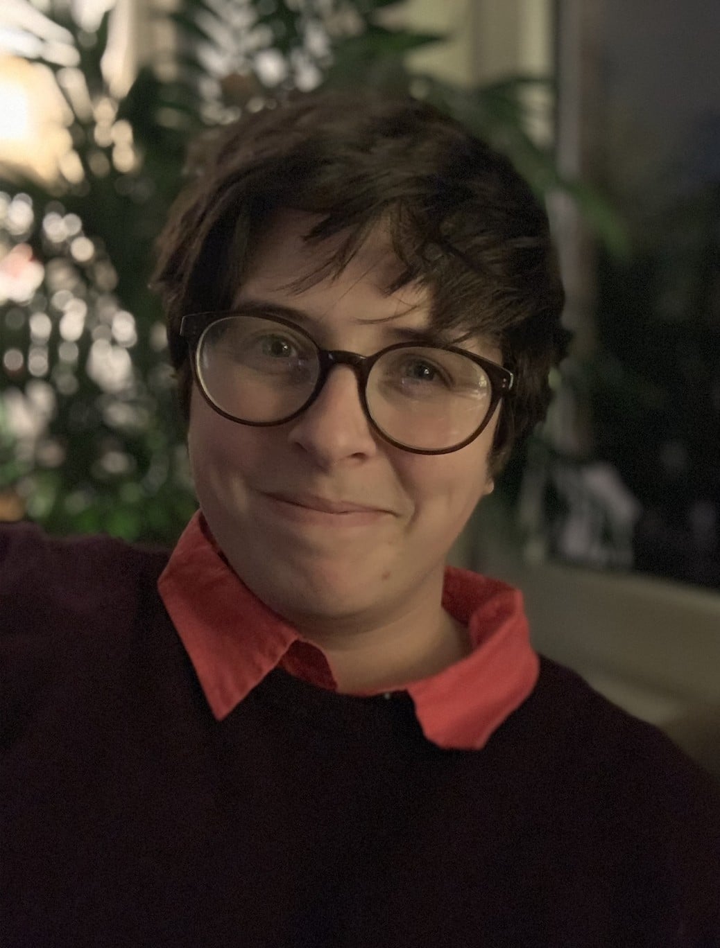 A headshot of a person with short hair and wearing a dark jumper and glasses