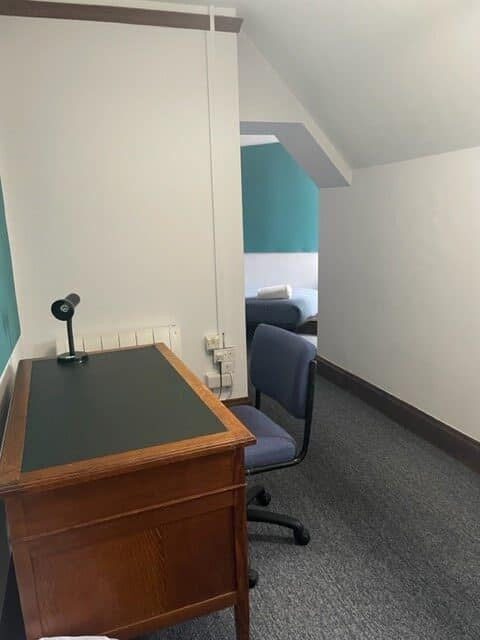 Room with desk and chair, leading to an area with single bed