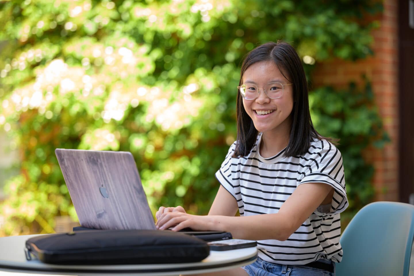 a young person sat in an outdoor location typing on a laptop