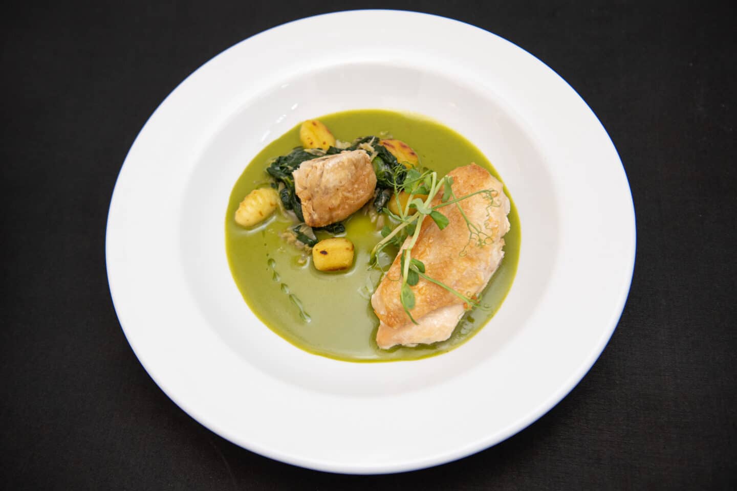 A plated dinner with chicken, gnocchi and sauce