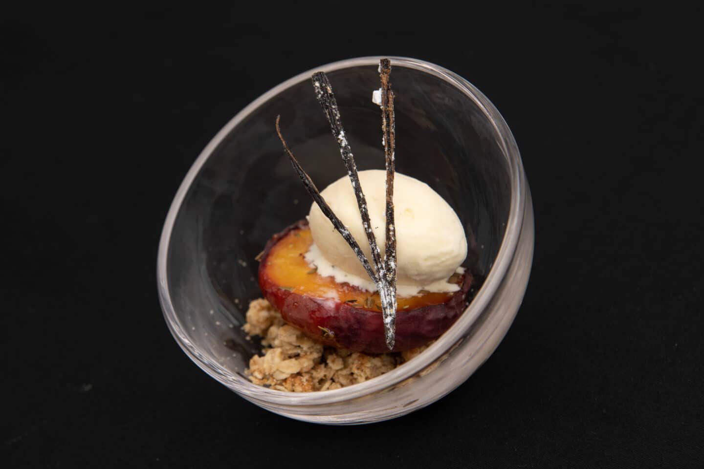 A dessert dish with fruit, ice cream and vanilla bean garnish