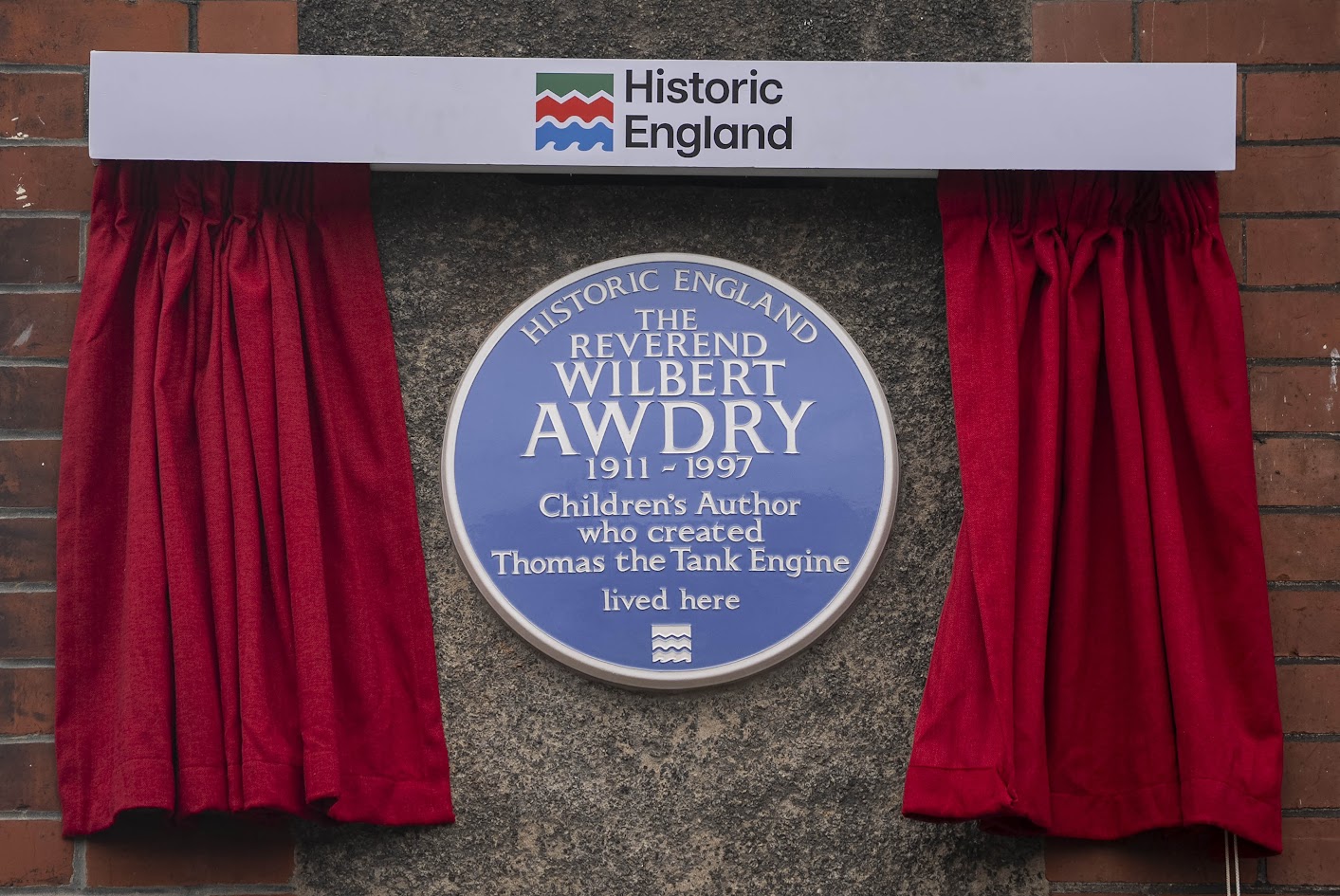 A blue plaque and red curtains on a wall.