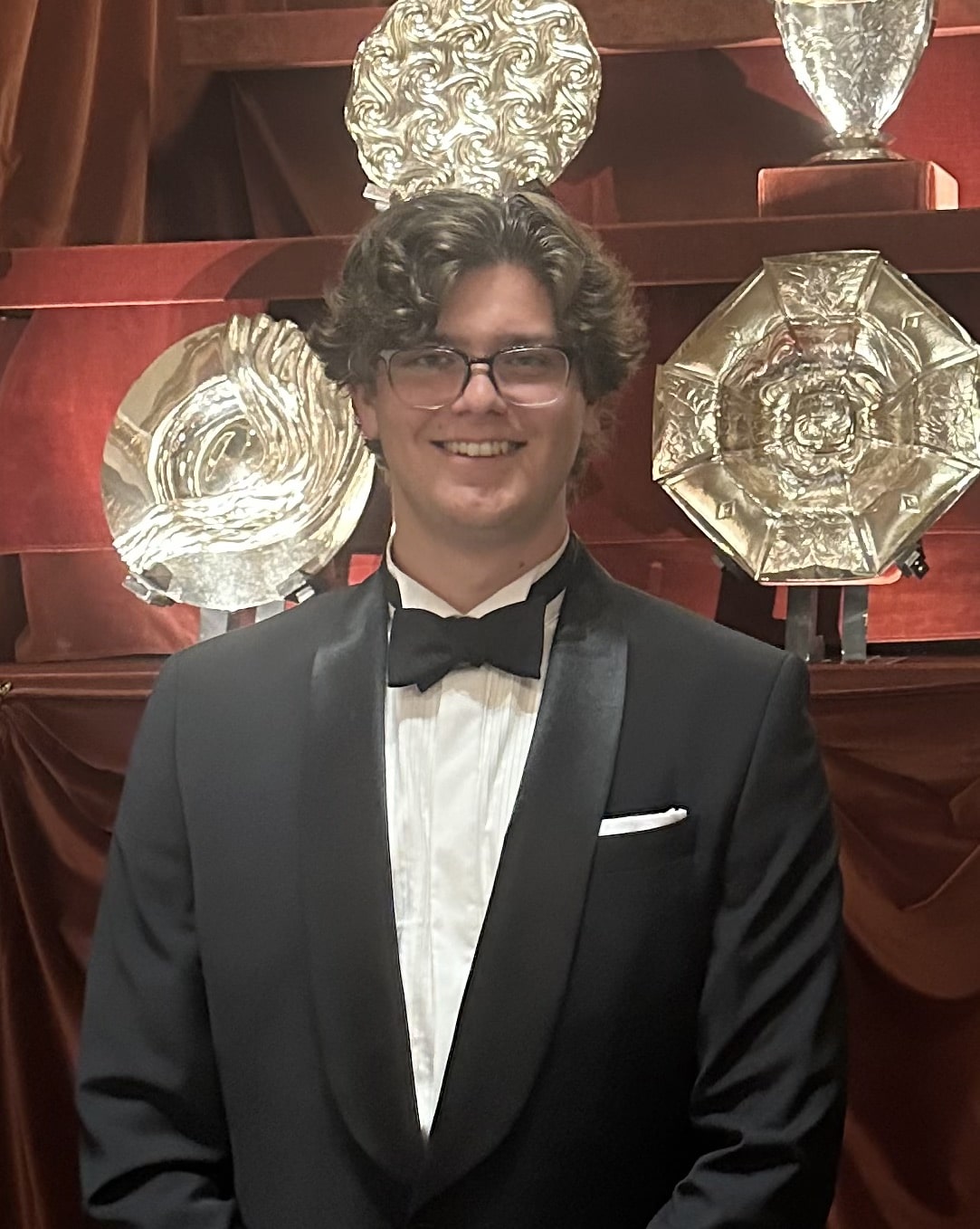 A student in black tie in front of four mounted silver plates