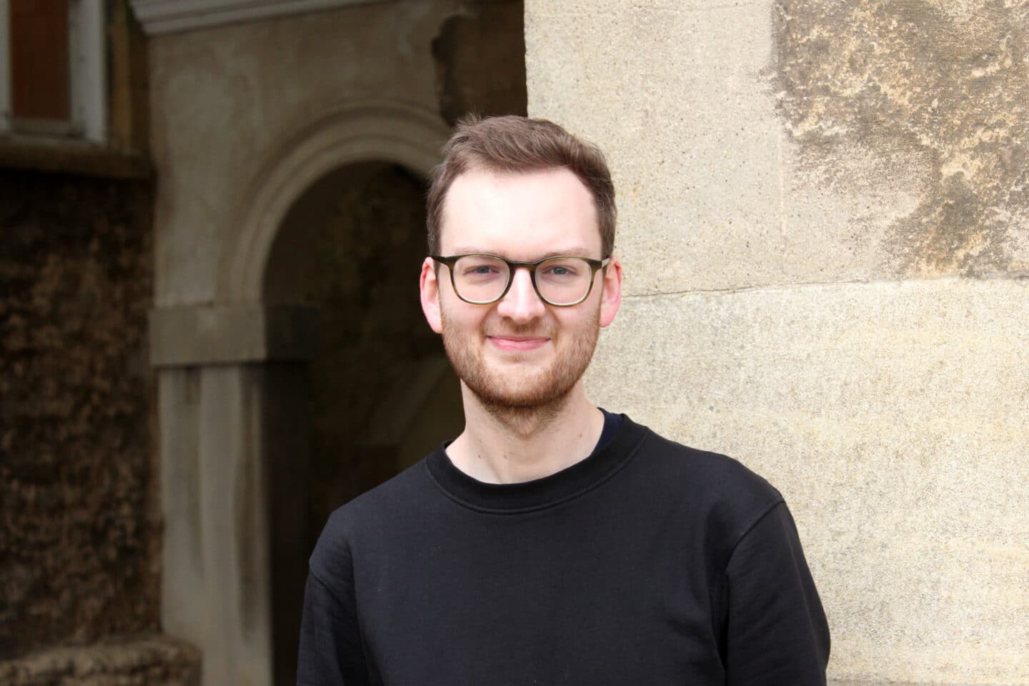 A headshot of a person wearing a black jumper and glasses