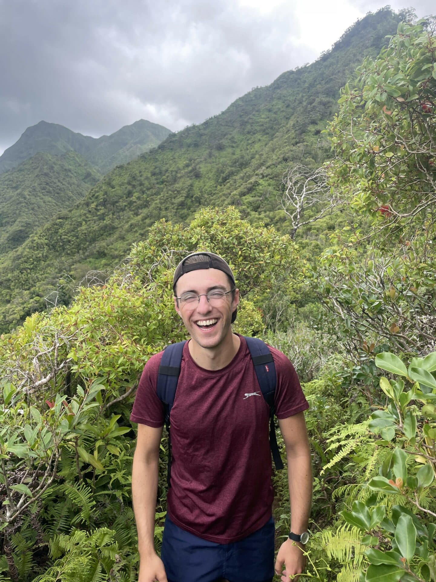 A person wearing outdoor walking gear in a tropical setting surrounded by green mountains