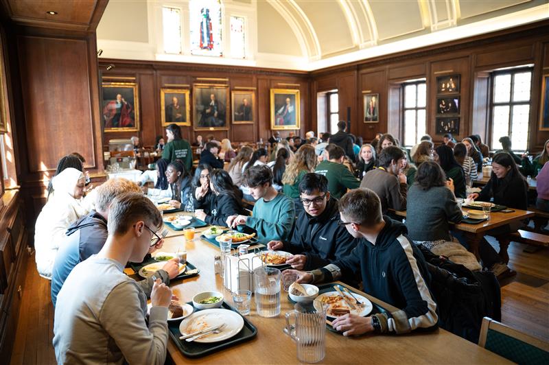 Young people sitting at long tables eating in the dining hall