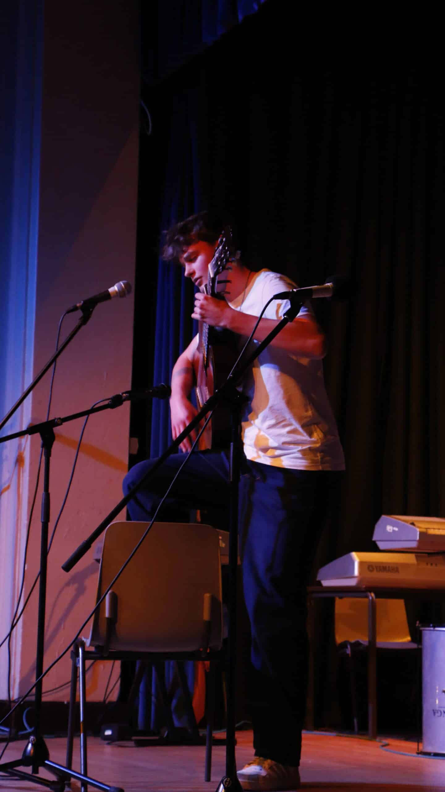 A seated student at a microphone playing the guitar
