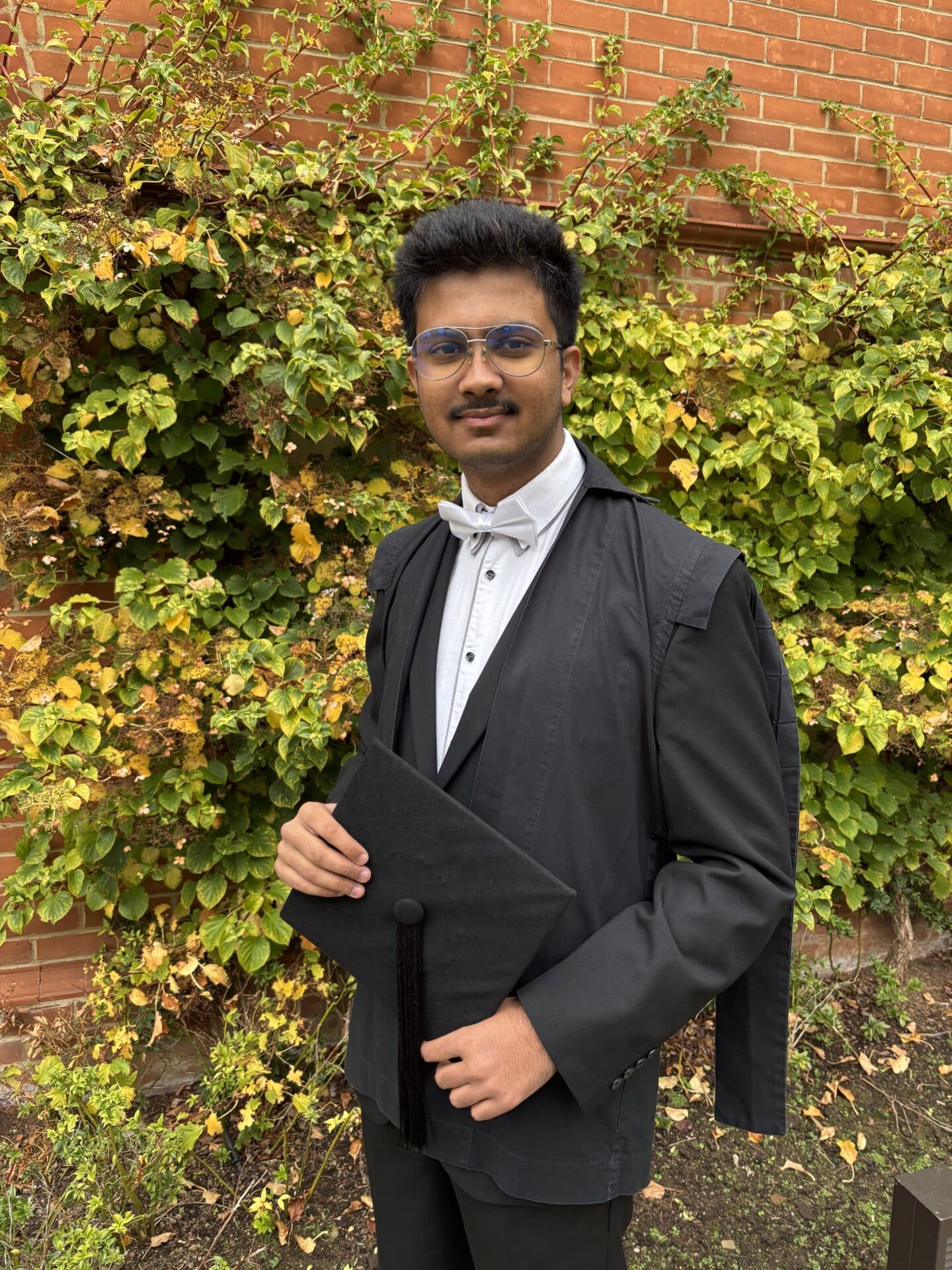 A student in sub fusc against a background of ivy leaves