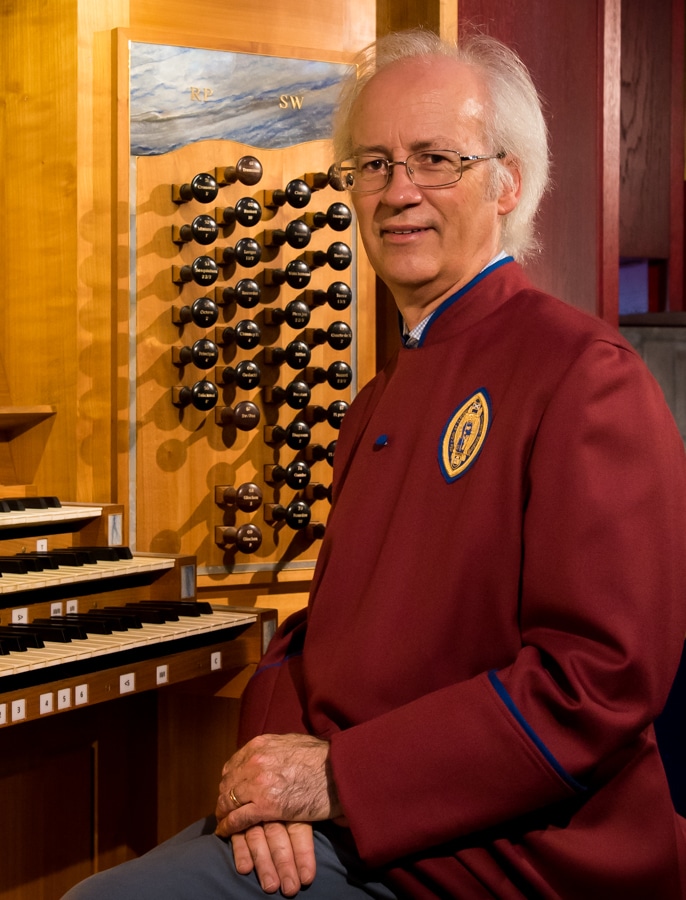 A man wearing a red jacket and glasses seated at an organ