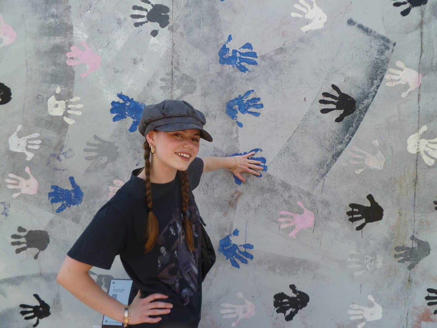 A young person stood by a concrete wall covered in painted handprints