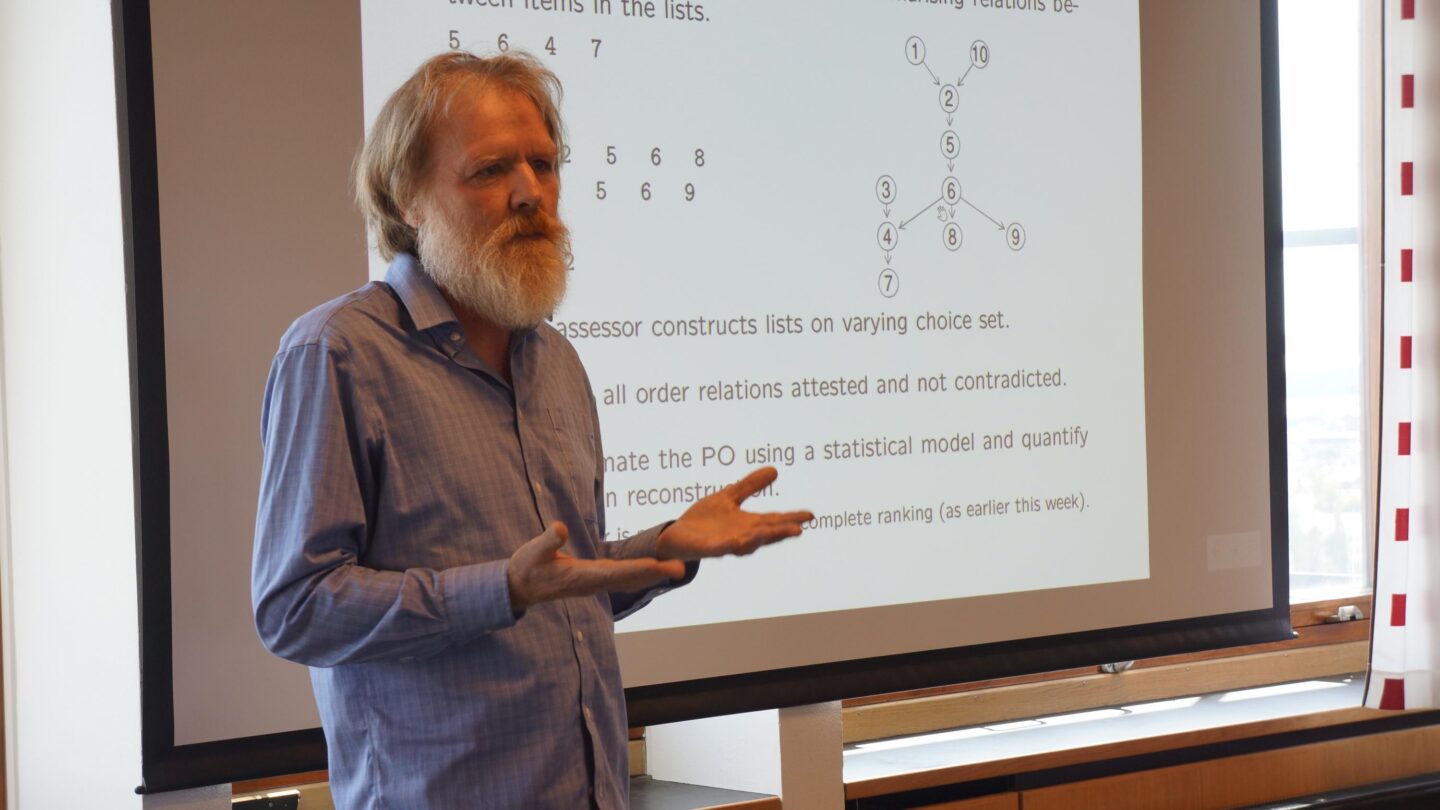 Headshot of Prof Geoff Nicholls lecturing in front of a screen