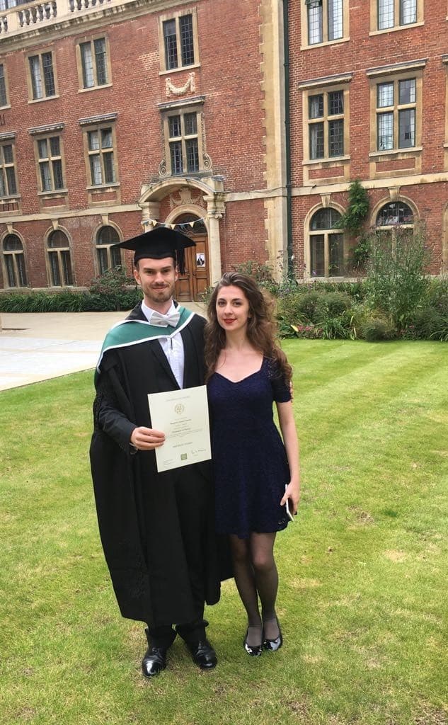 A couple standing outdoors wearing formal clothing and holding a diploma