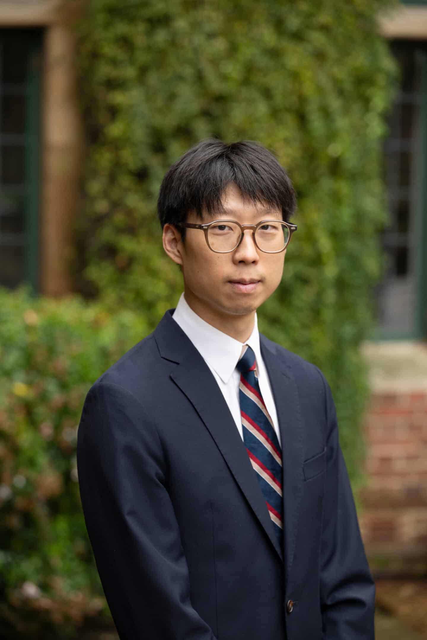 A man wearing a blue suit and glasses standing outside