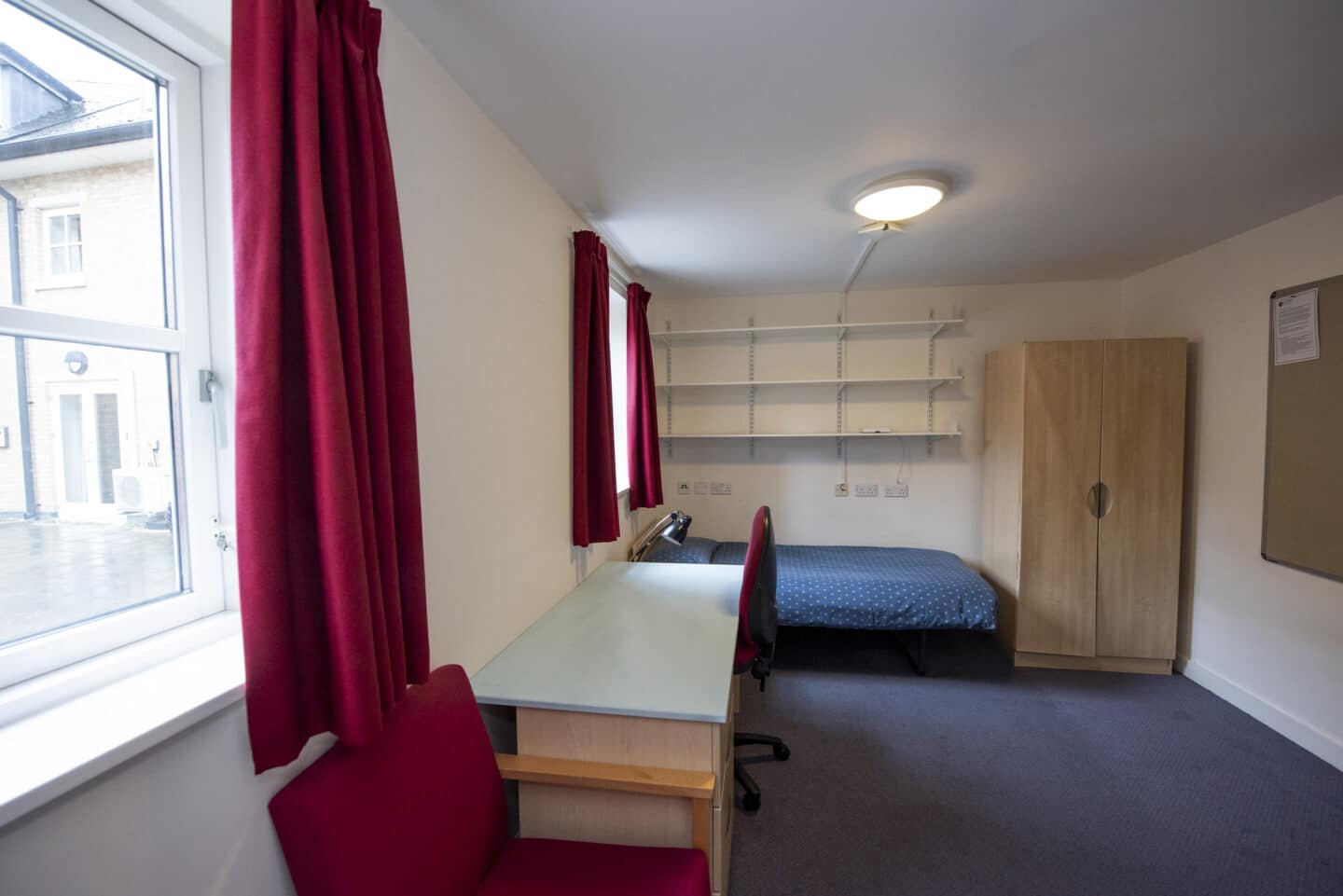 A spacious room furnished with shelves, a bed, a desk and chairs