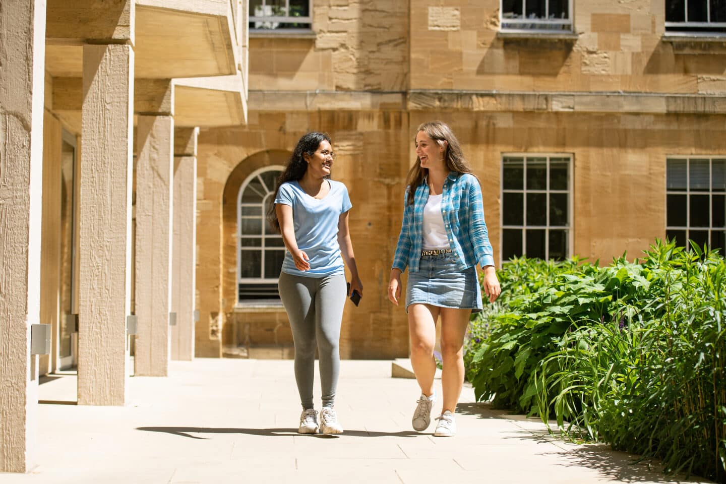 Two women walking in a sunny college quad