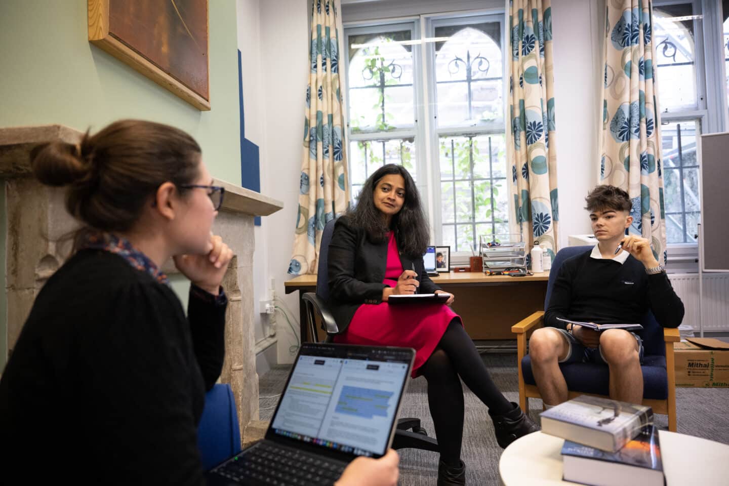 Three people sitting in an office with computers and notebooks