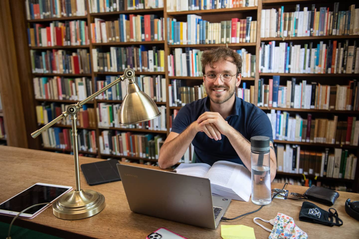 A student sitting at a library table with a textbook and computer