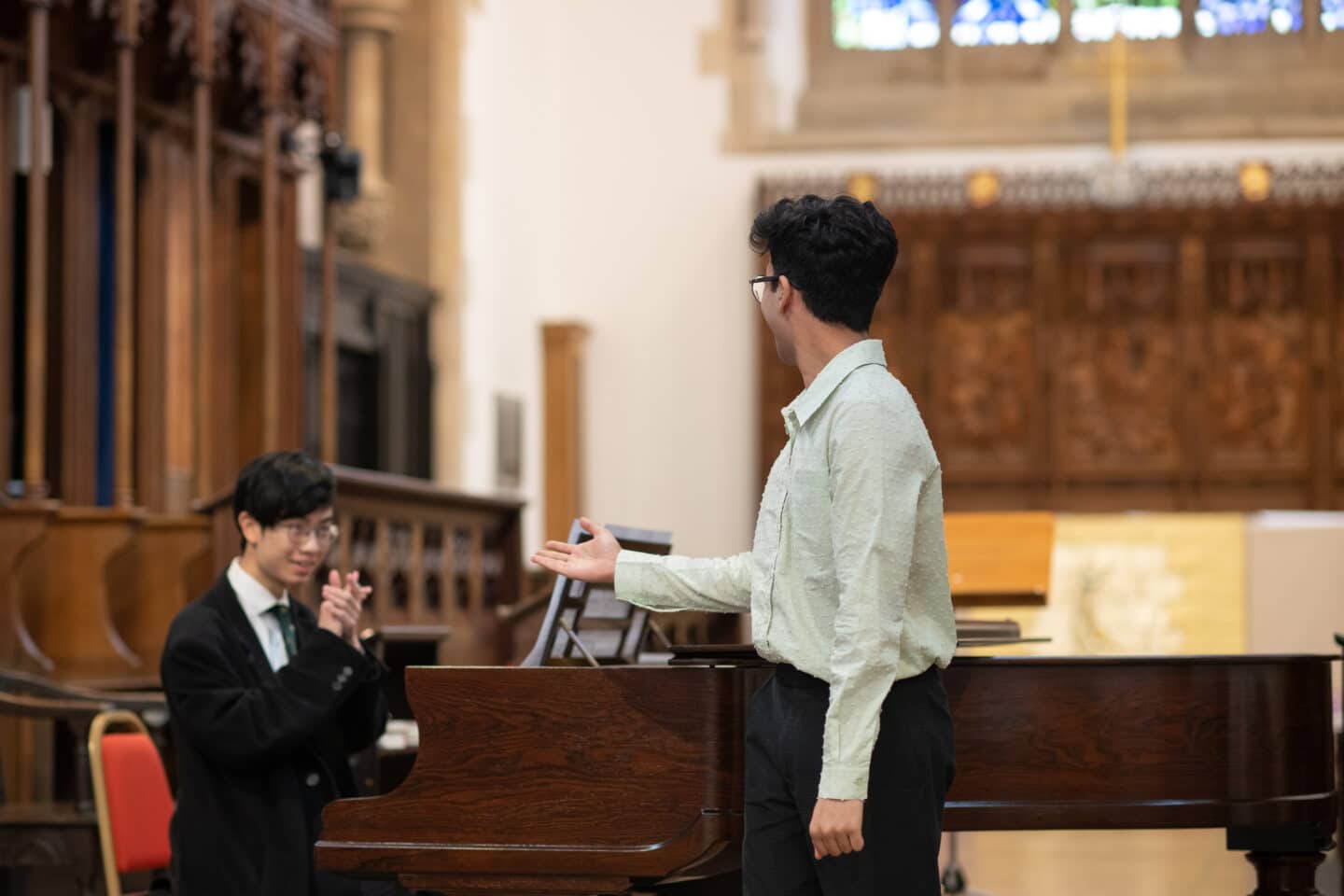 A singer standing in a chapel, with a pianist at a piano behind him