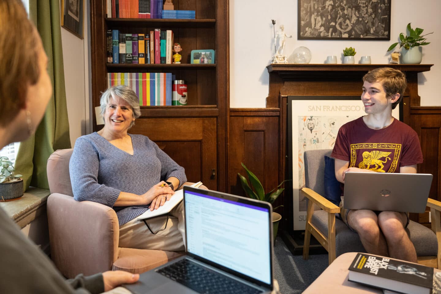 Two students holding computers and speaking to their tutor in an office