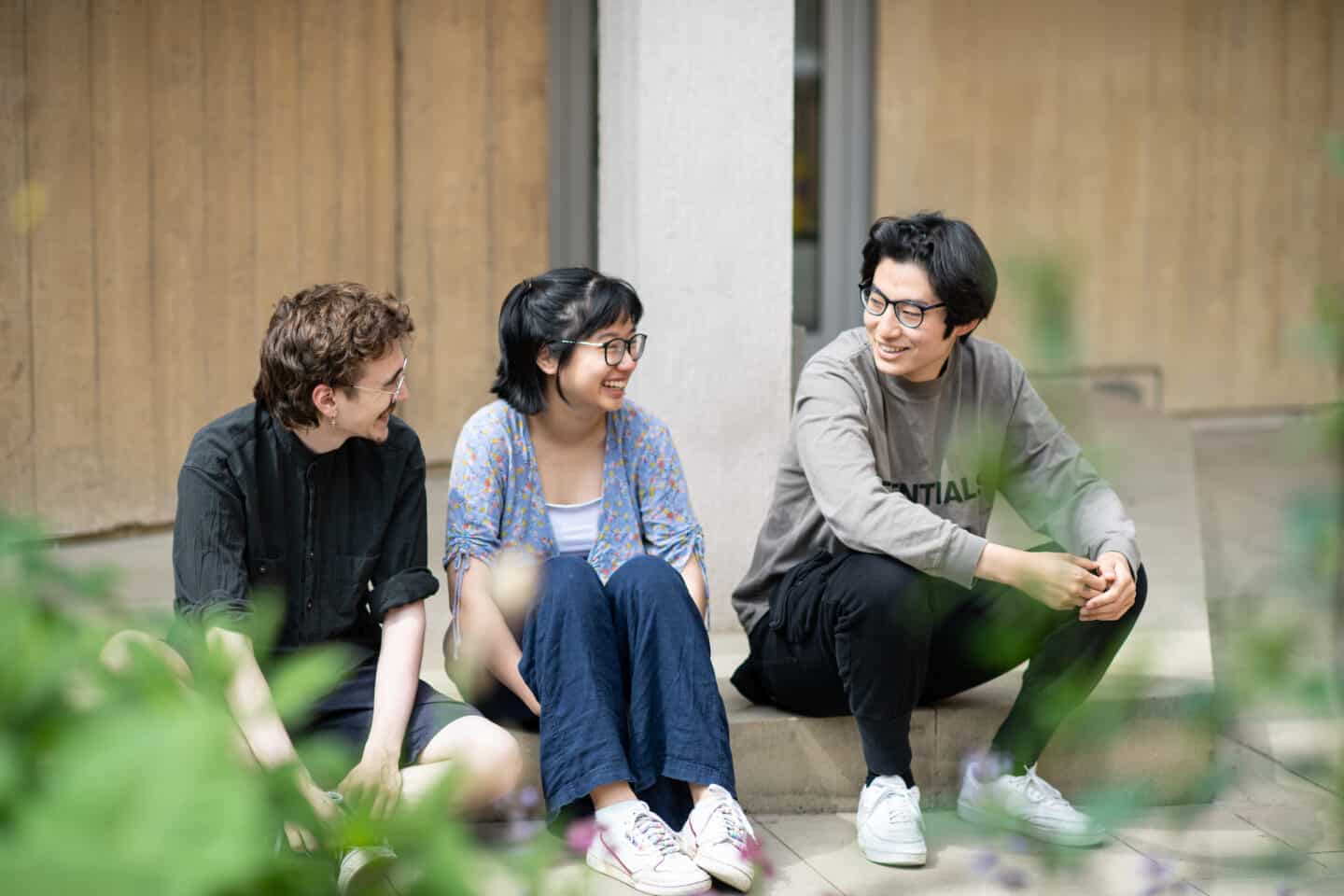 Three students sitting on an outdoor step and smiling