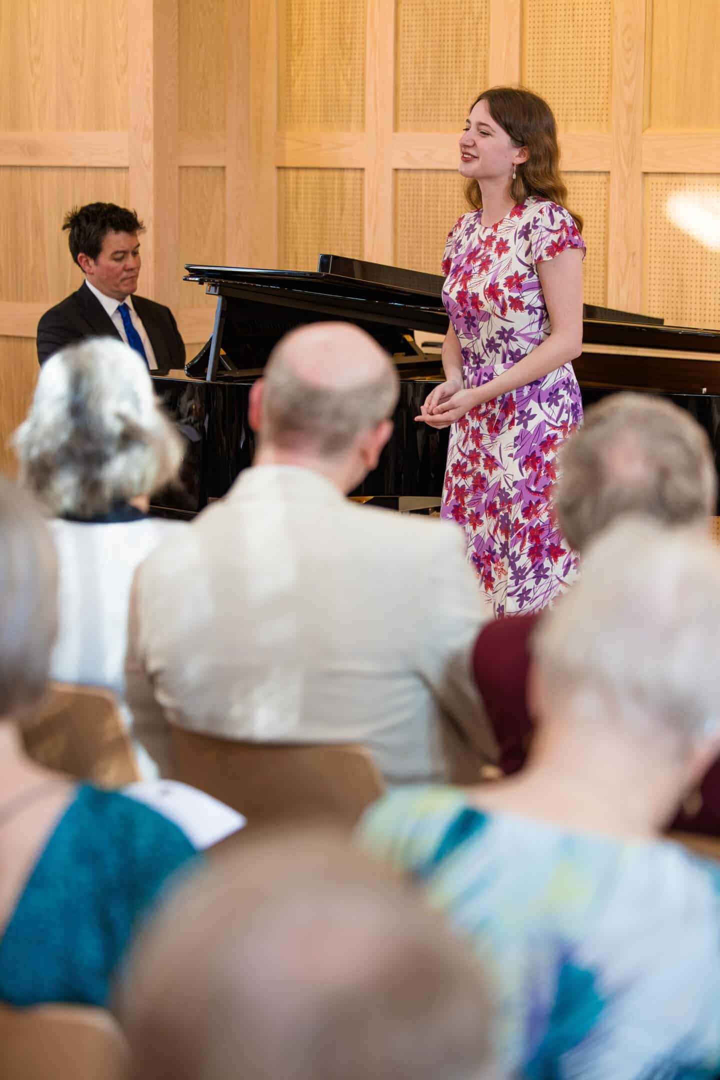 A man playing a small grand piano and a woman playing the trumpet in a wood-paneled room filled.