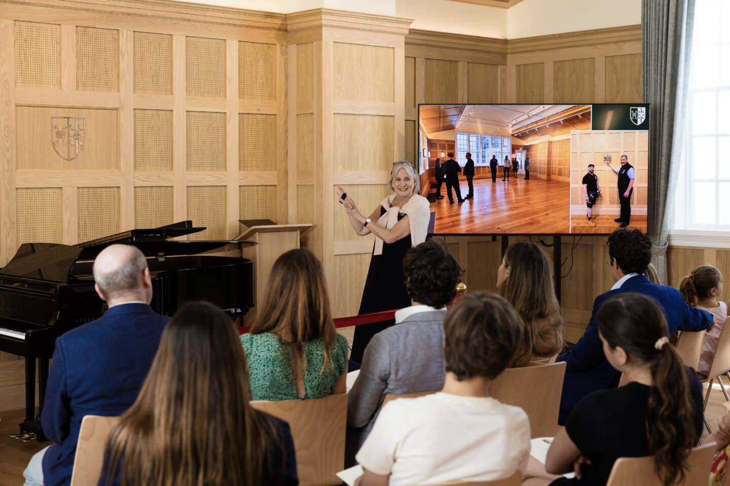 A woman showing a powerpoint in a wood-panelled room.