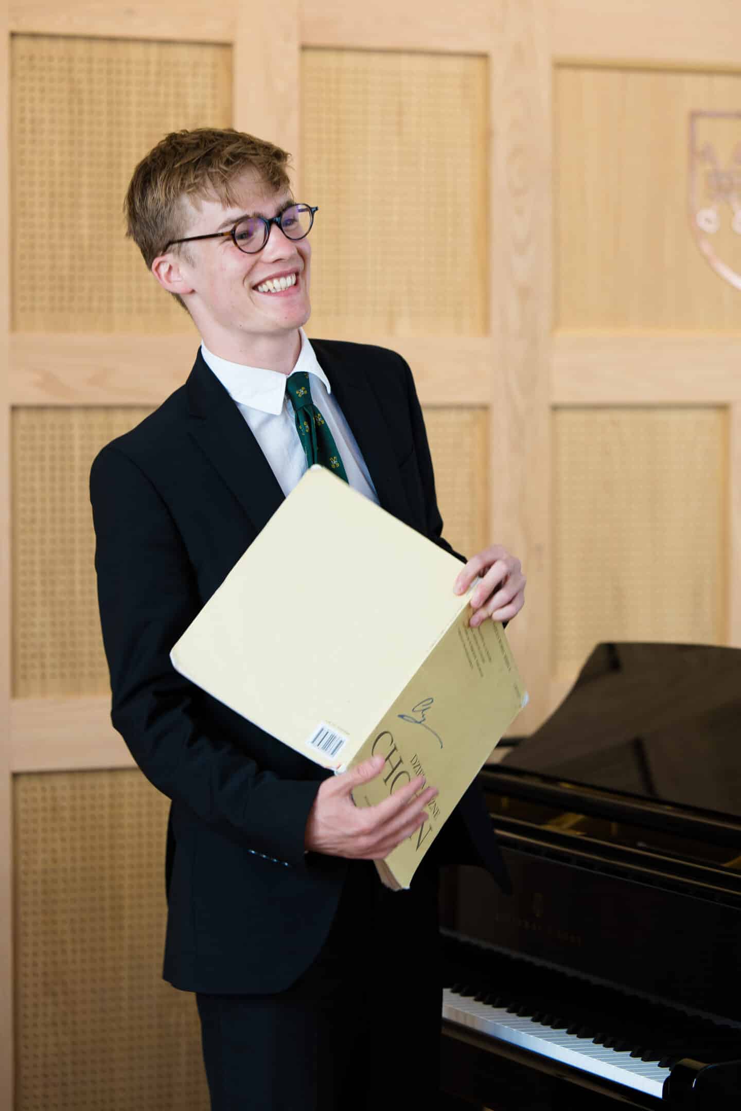 A young man holding a musical score in front of a Steinway piano