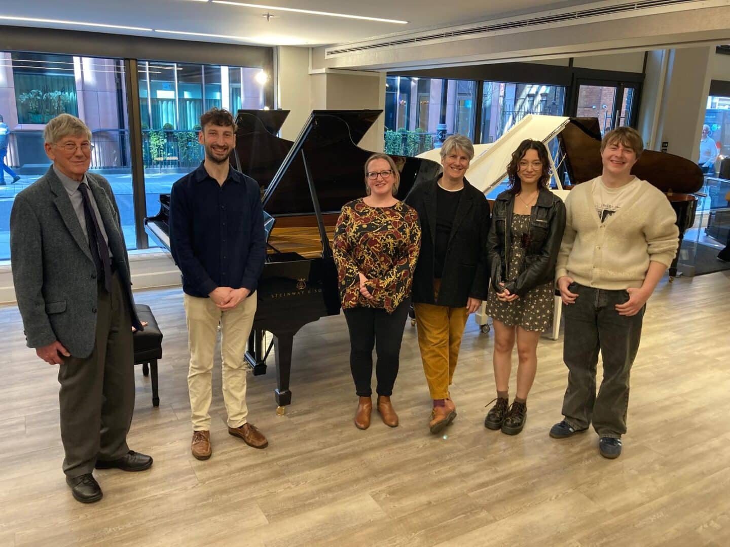 a group of six people standing in a piano showroom by a grand piano
