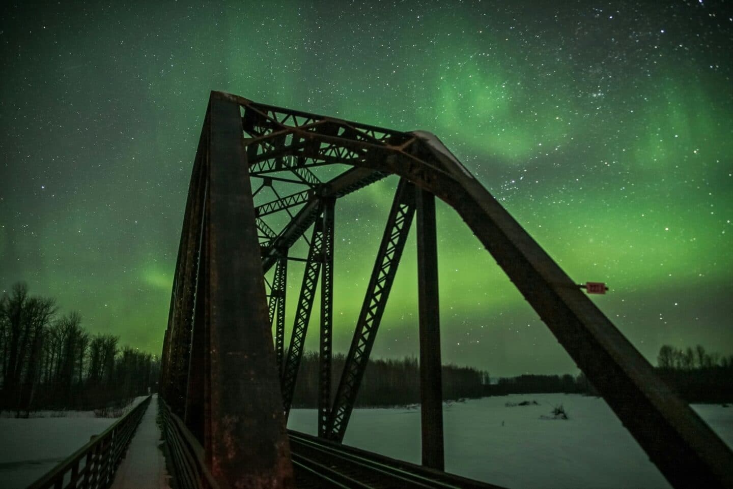 A steel rail bridge with green northern lights in the background