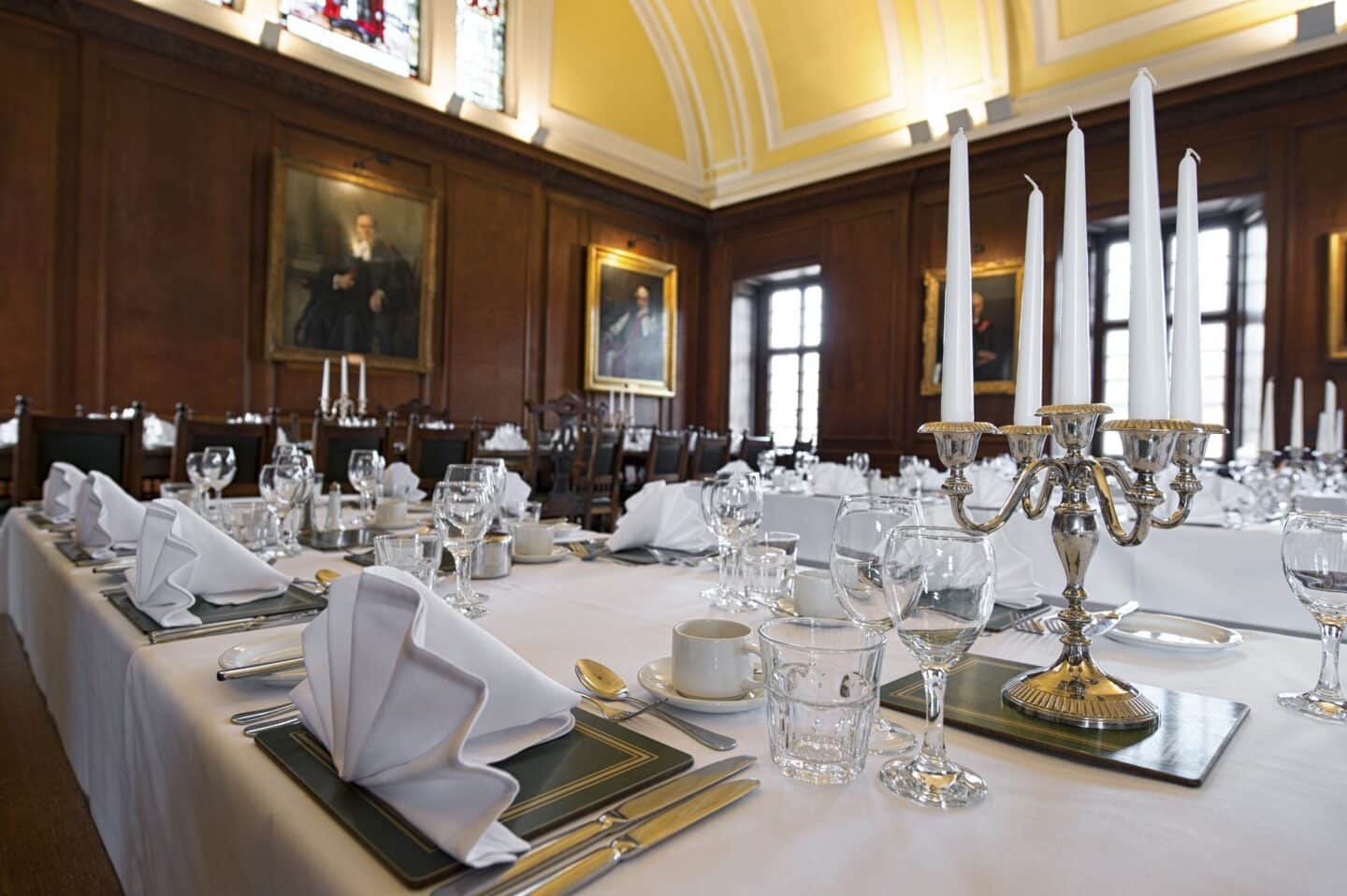 A table set for a formal dinner in a large and old dining hall