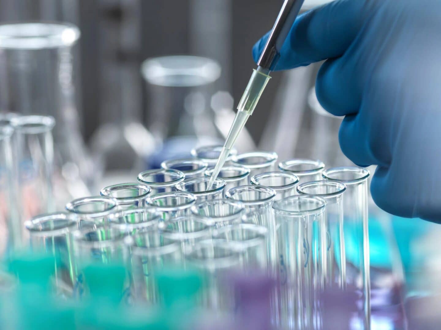 A gloved hand using a pipette to add something to a test tube