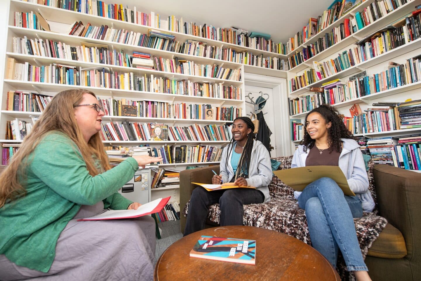 a woman teaching two students in an office filled with books