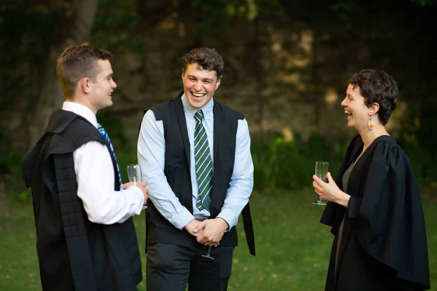 a group of three people smiling and wearing academic gowns outside in a garden