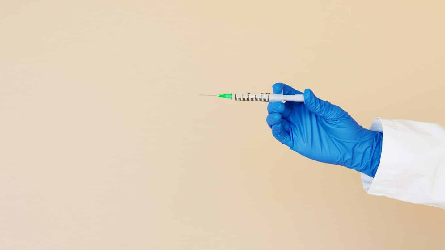 a hand in a blue glove holding a syringe