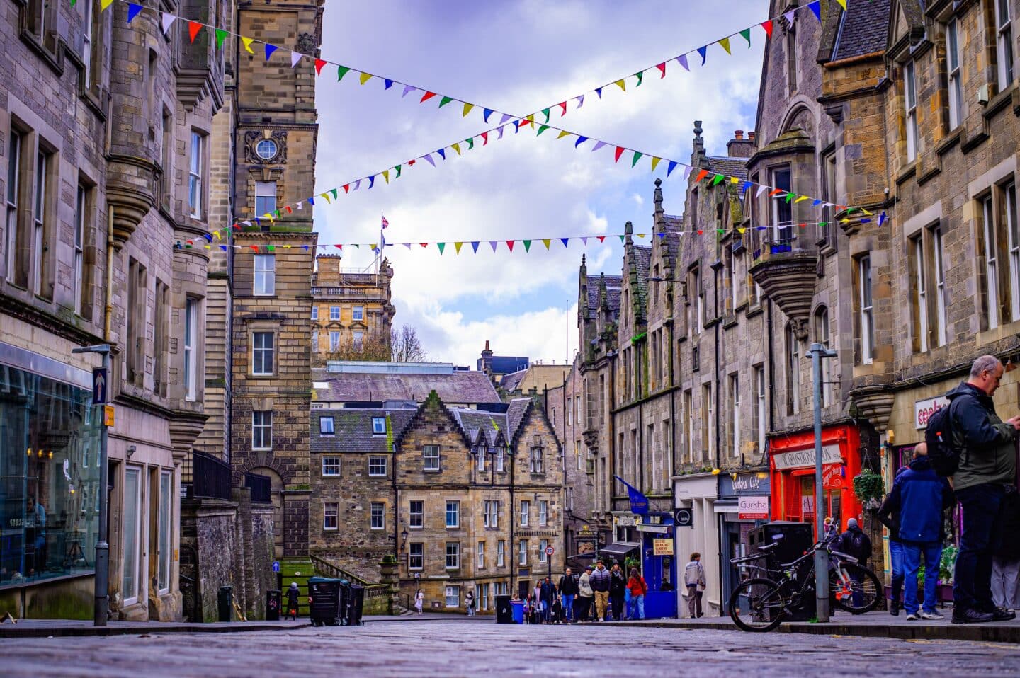 A busy street in Edinburgh with bunting, shops, and old stone buildings