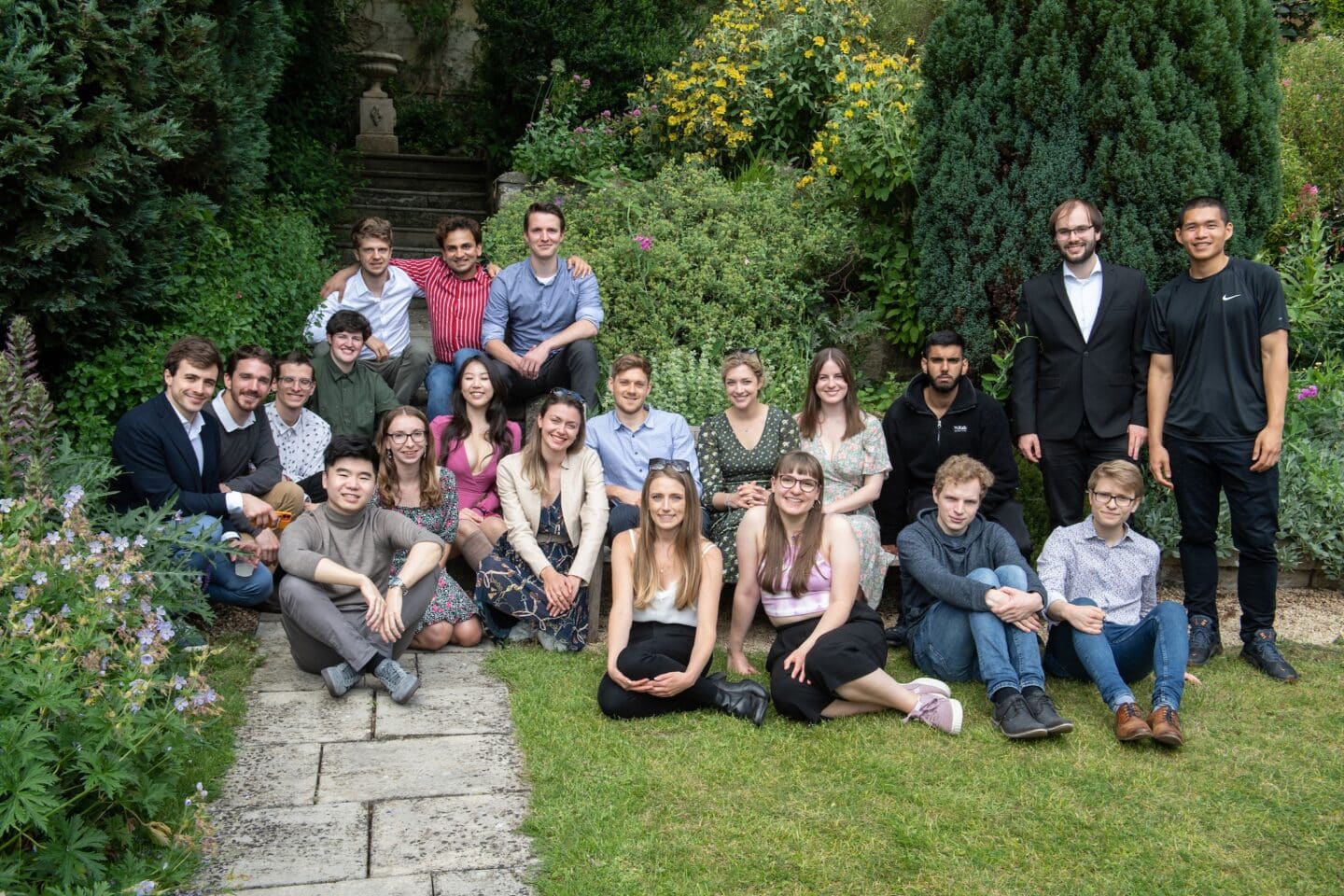 a large group of postgraduate students posing and smiling in a garden