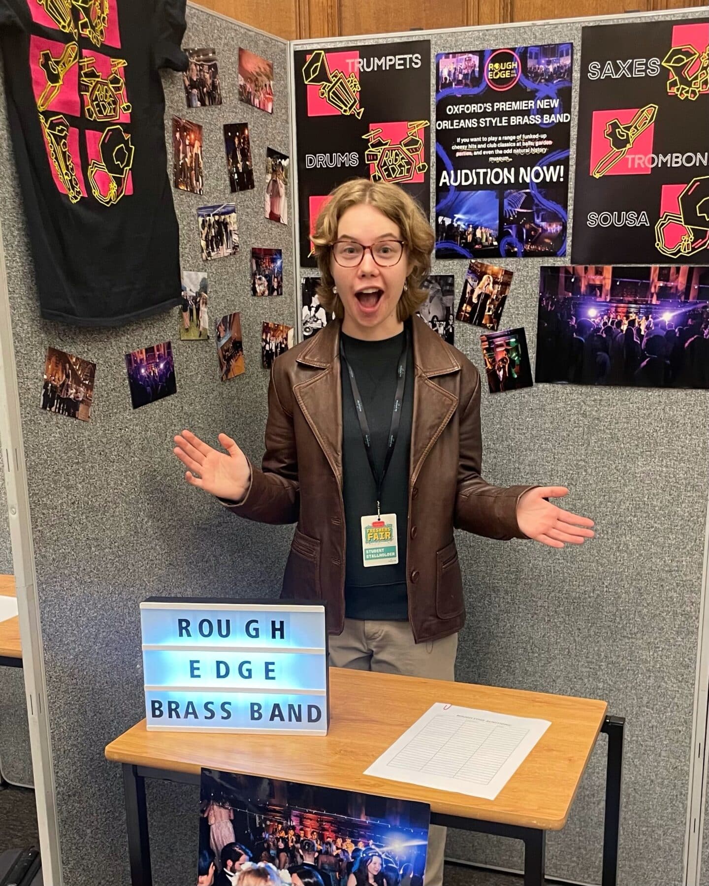 A student standing behind a desk, with a sign saying "rough edge brass band"