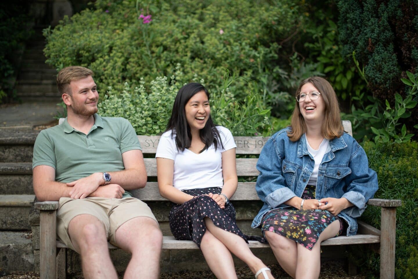 three students sitting on a bench in a garden